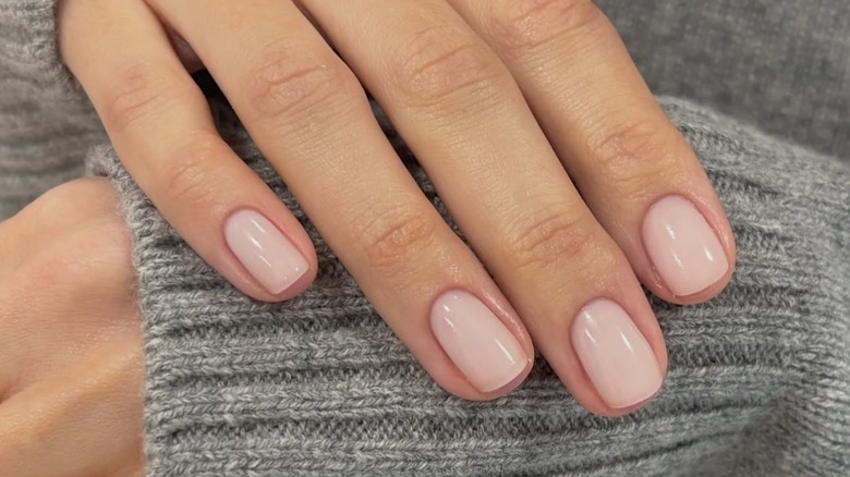 La main d'une femme montrant sa manucure nue sur un pull gris