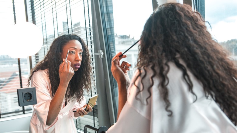 Une femme appliquant du fard à paupières avec un pinceau tout en se regardant dans un miroir