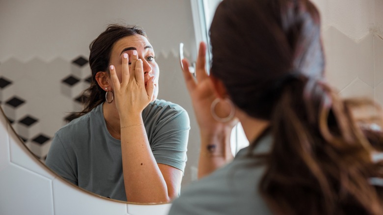 Une femme touchant sa paupière avec son doigt tout en se regardant dans un miroir