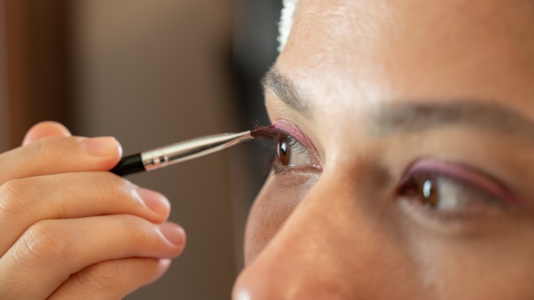 Une femme appliquant un fard à paupières rose sur les yeux cagoulés