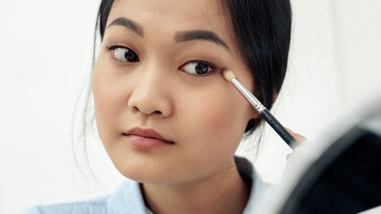 Une femme appliquant du fard à paupières sur ses yeux avec un petit pinceau