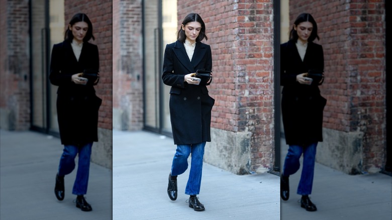 Une femme marchant dans la rue portant un manteau, un jean bleu et des chaussures derby