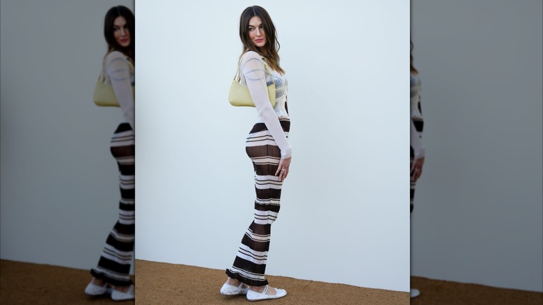 Une femme vêtue d'une robe rayée avec un pull blanc et des chaussures plates