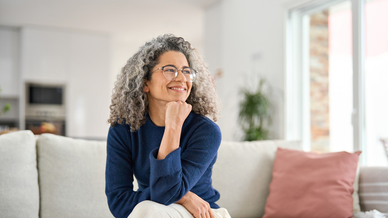 femmes aux cheveux gris bouclés souriant dans un pull à col rond bleu