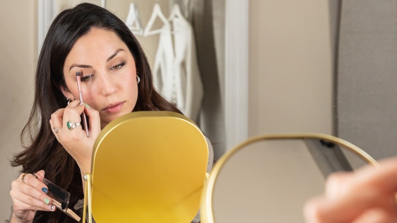 Une femme appliquant un fard à paupières plus foncé sur ses yeux tout en se regardant dans un miroir