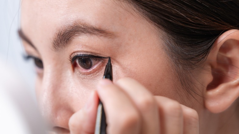 Une femme appliquant un eye-liner noir sur sa paupière supérieure