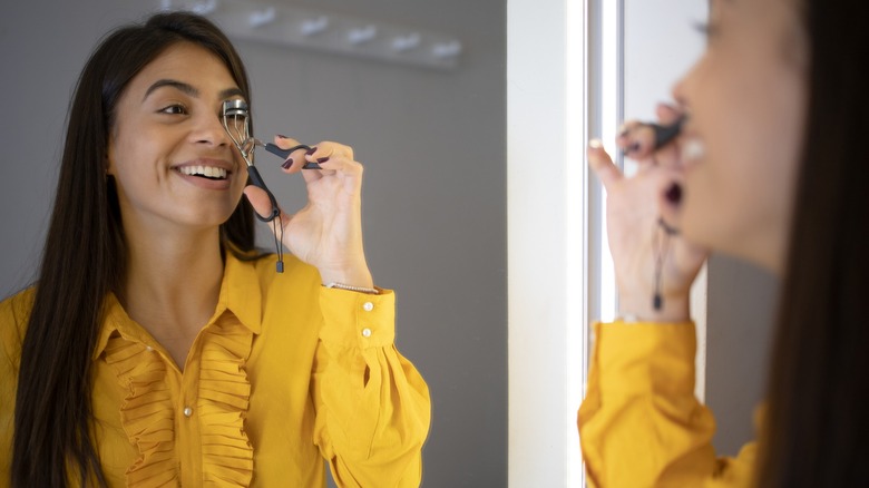 Une femme souriant dans le miroir tout en frisant ses cils