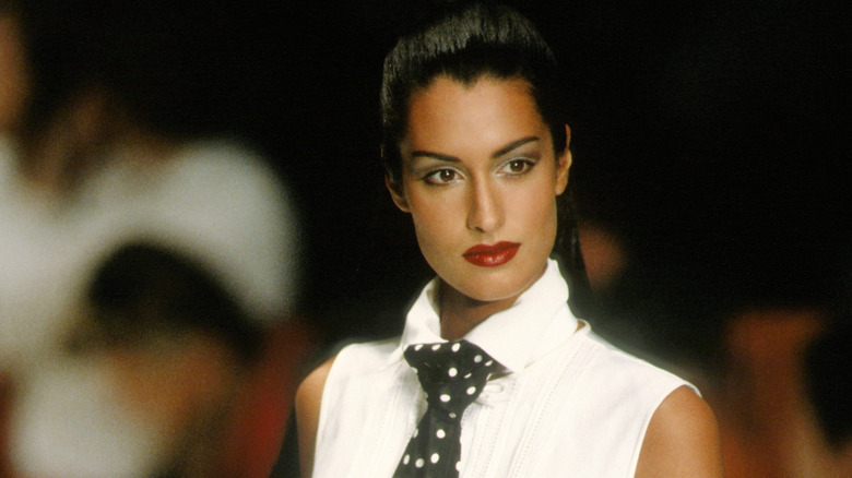 Yasmeen Ghauri dans un chemisier blanc sans manches avec une cravate à pois et un rouge à lèvres rouge