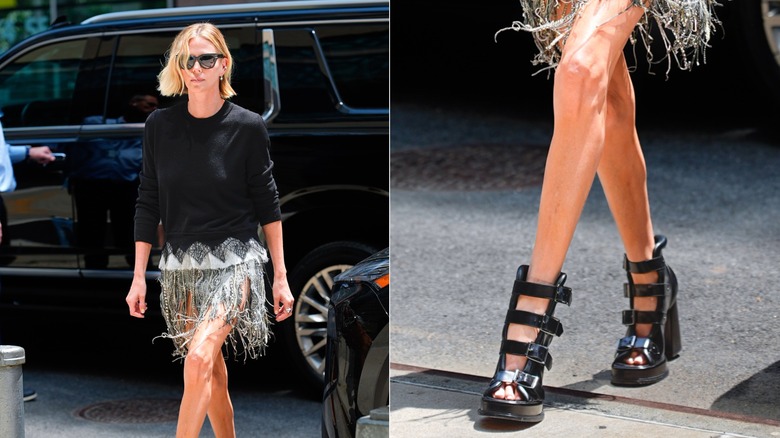 Charlize Theron marchant avec une jupe à franges, un pull noir et de grosses sandales à boucles