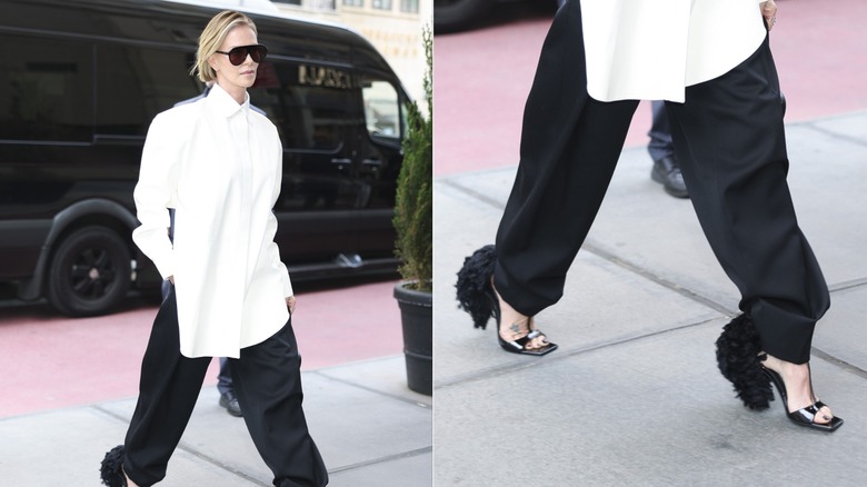 Charlize Theron marche vêtue d'une chemise blanche et d'un pantalon noir avec des talons noirs à plumes