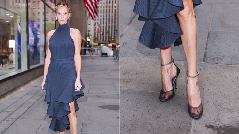Charlize Theron pose vêtue d'une robe bleu marine à col roulé avec une jupe à volants et des talons noirs transparents
