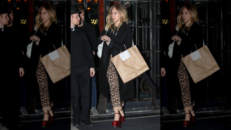Juno Temple en pantalon imprimé léopard et manteau noir avec des chaussures rouges