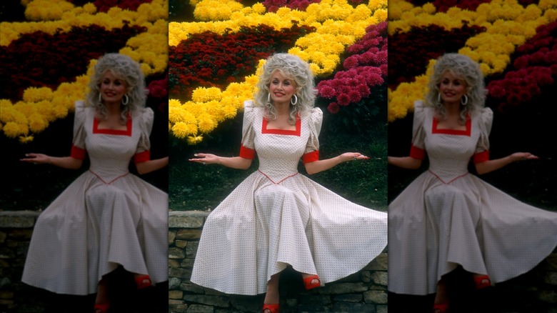 Dolly Parton assise sur un mur dans une robe blanche et rouge