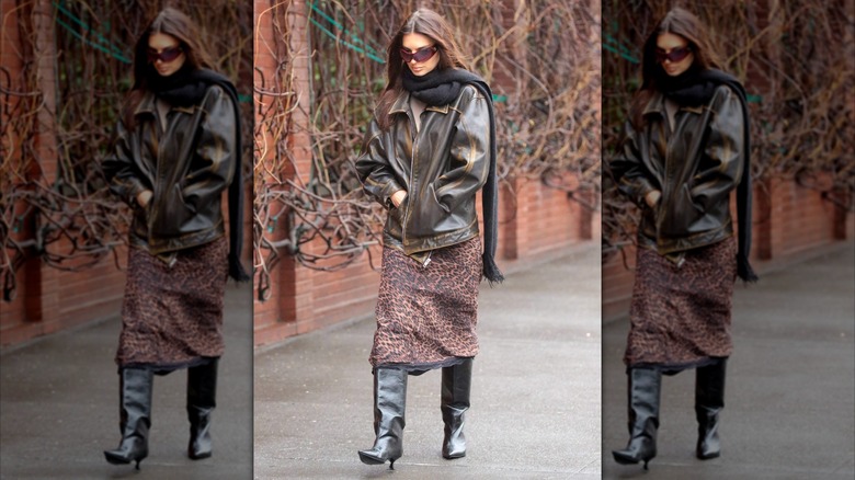 Emily Ratajkowski photographiée portant une jupe à imprimé jaguar avec des bottes noires et une veste en cuir