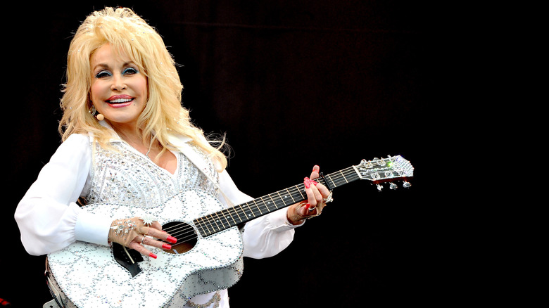 Dolly Parton joue de la guitare sur scène en blanc avec une guitare blanche