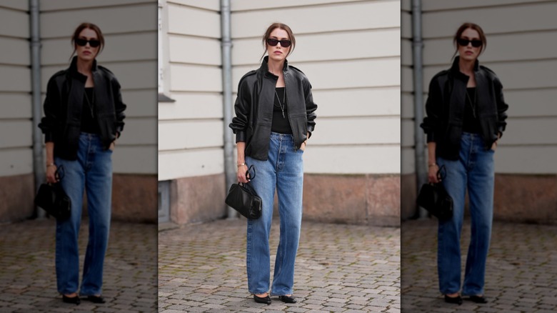 Une femme debout dans la rue en jean droit et une veste en cuir