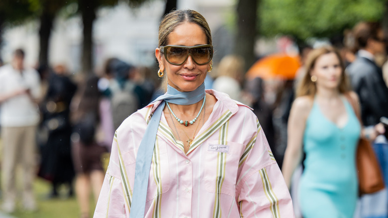 Tiany Kiriloff porte un chemisier rose, une robe à franges jaune turquoise, un sac bleu et des lunettes de soleil à l'extérieur