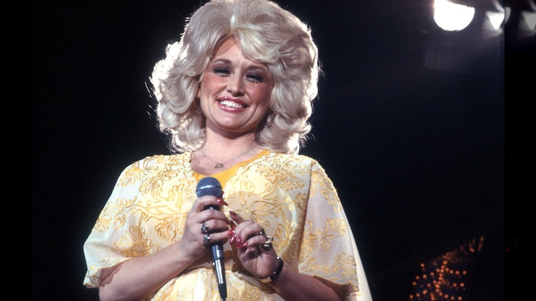 Dolly Parton en jaune avec des ongles rouges tout en tenant un microphone
