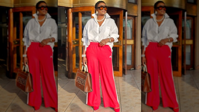 Une femme en pantalon de survêtement rouge et un chemisier blanc avec un gros collier de perles