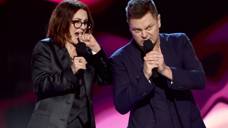 Megan Mullally portant un blazer noir et Nick Offerman portant un costume bleu avec un collier en or