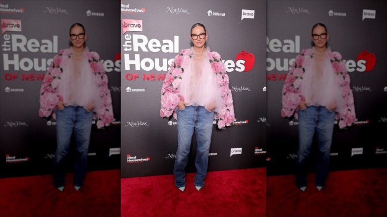 Jenna Lyons pose portant une veste surdimensionnée à fleurs rose et un jean en denim