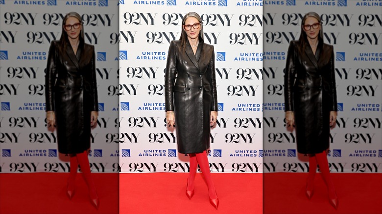 Jenna Lyons pose avec les jambes croisées portant une longue veste en cuir et des collants rouges