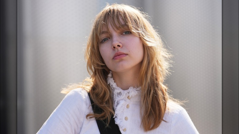 Une femme posant dans une chemise blanche avec une expression neutre et une frange complète