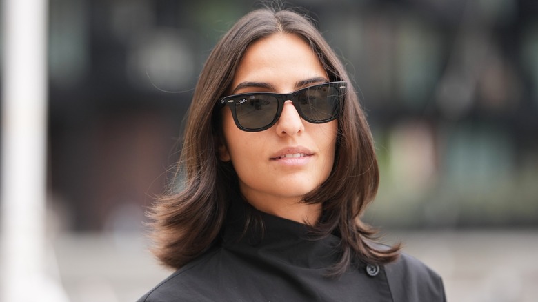 Une femme à l'expression neutre portant des lunettes de soleil avec une coupe de cheveux lobée