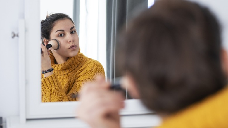 Une femme appliquant de la poudre dans le miroir