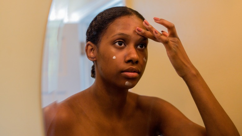 Une femme se regardant dans le miroir tout en appliquant une base pour le visage