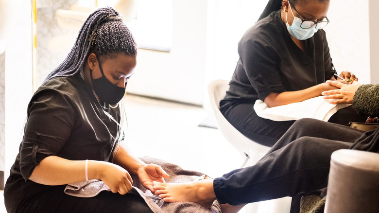 Manucure en gommages noirs travaillant sur les pieds des clients