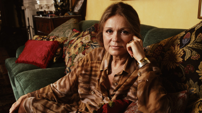 Gloria Steinem était assise sur un canapé vert et portait une blouse marron