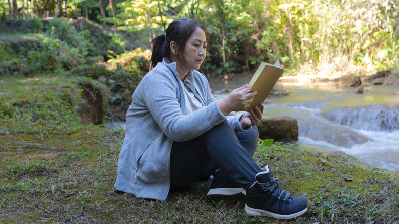 Femme lisant dans les bois près d’un ruisseau