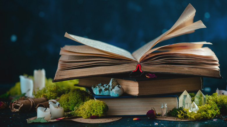 Pile de livres avec des cristaux, des herbes, des bougies et des bouteilles de potion