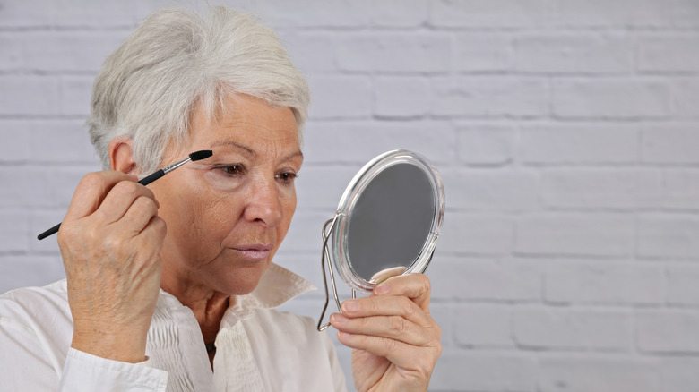 les femmes plus âgées regardent avec impatience dans un petit miroir portant une chemise blanche