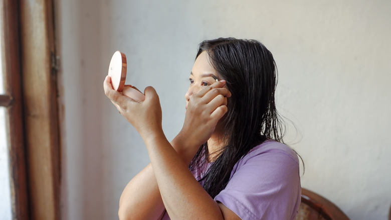 les femmes plus âgées regardent avec impatience dans un petit miroir portant une chemise rose