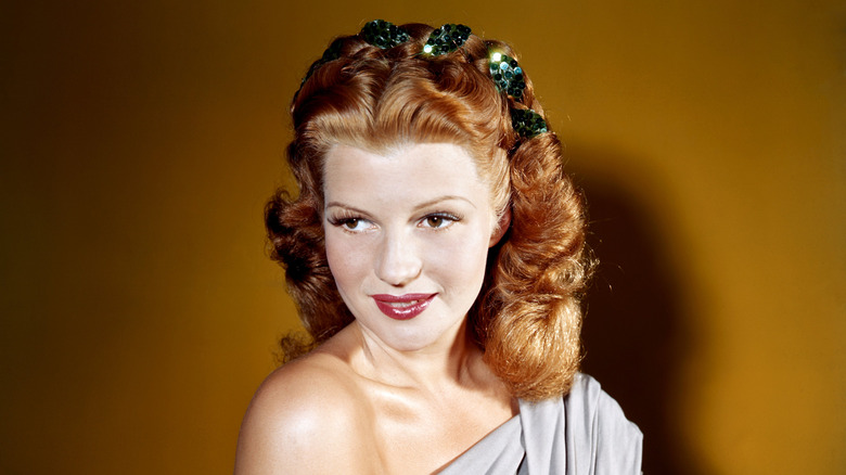 Rita Hayworth sourit avec des cheveux roux et porte du rouge à lèvres