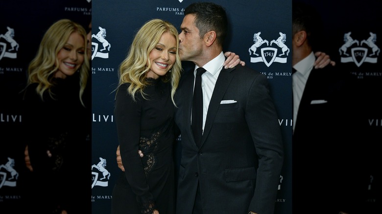 Kelly Ripa souriant et Mark Consuelos lui faisant un bisou sur la tempe