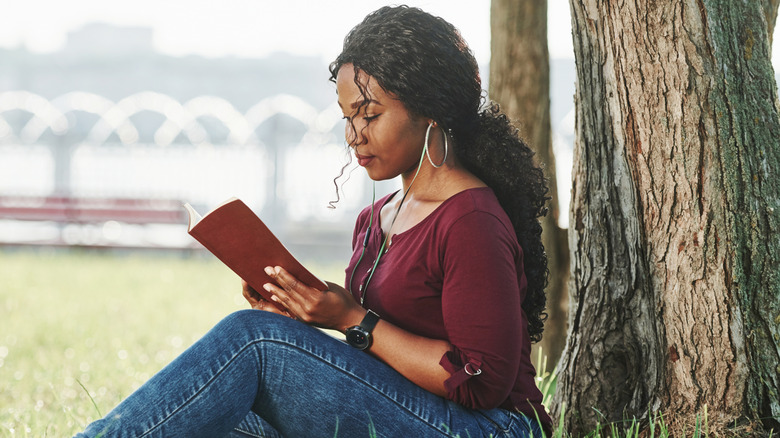 Femme assise dans l'herbe contre un arbre en train de lire