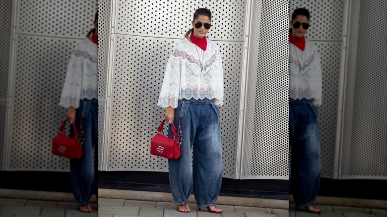Une femme portant un jean canon et un haut blanc en dentelle avec un sac à main rouge