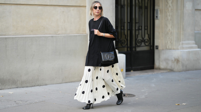 Femme marchant dans un grand t-shirt noir et une jupe longue blanche à pois noirs