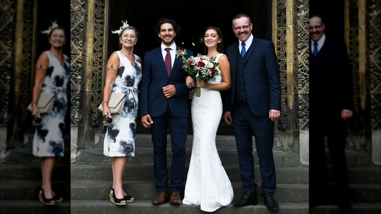 Un marié et une mariée debout avec leurs parents à l'entrée d'une église