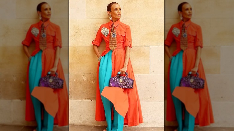 Une femme âgée élégante vêtue d'une robe orange ouverte avec un pantalon turquoise et un sac violet