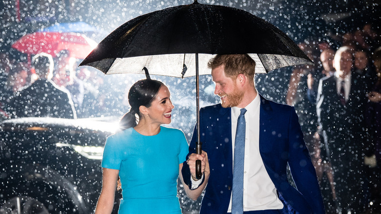 Meghan Markle en robe bleue marchant sous la pluie avec le prince Harry en costume bleu