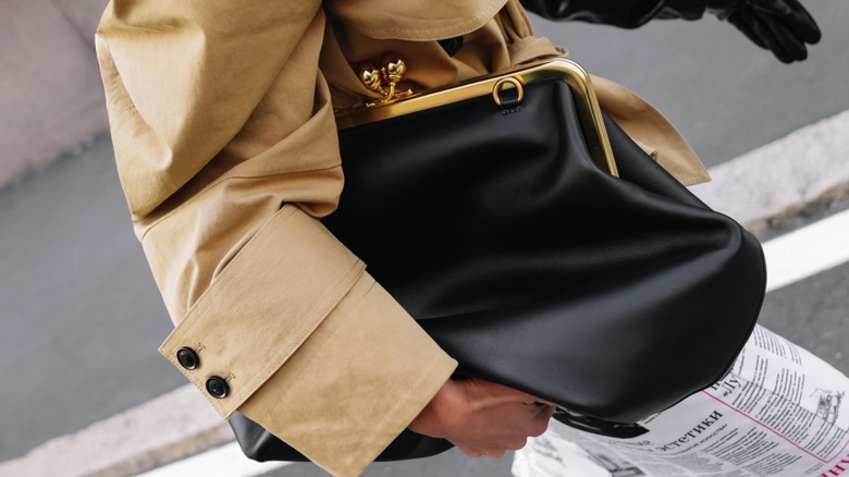 Une femme portant un sac kisslock noir sous le bras