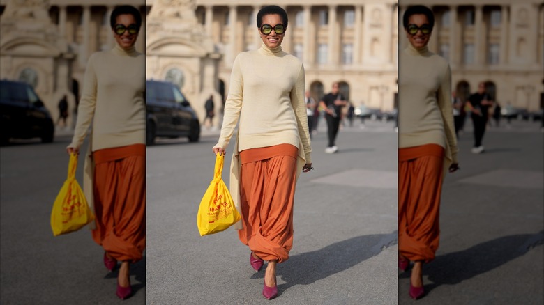 Une femme marchant dans les rues et souriante dans une jupe orange brûlée et un pull beige
