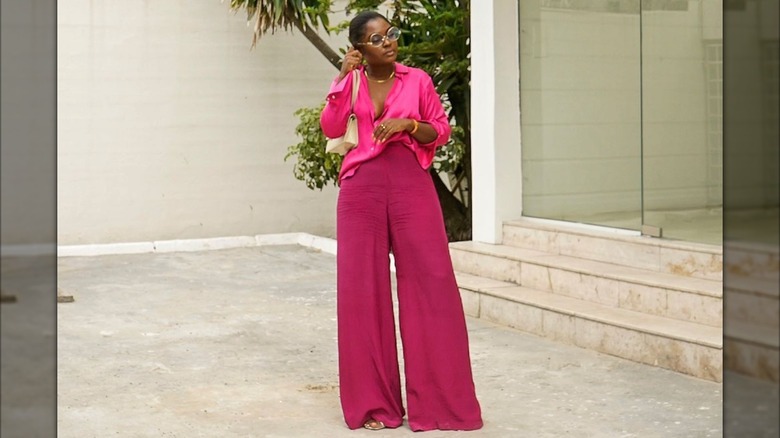 Une femme posant tout en portant un haut rose vif et un pantalon magenta foncé