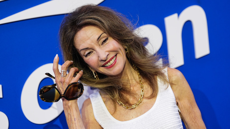 Susan Lucci dans une robe blanche et tenant des lunettes de soleil sur le tapis rouge
