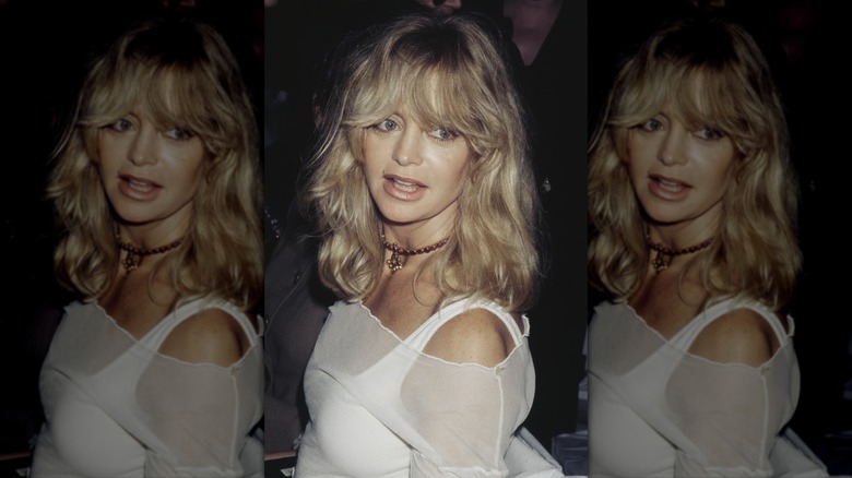 Goldie Hawn porte un haut blanc transparent à épaules dénudées avec des cheveux blonds et une frange.