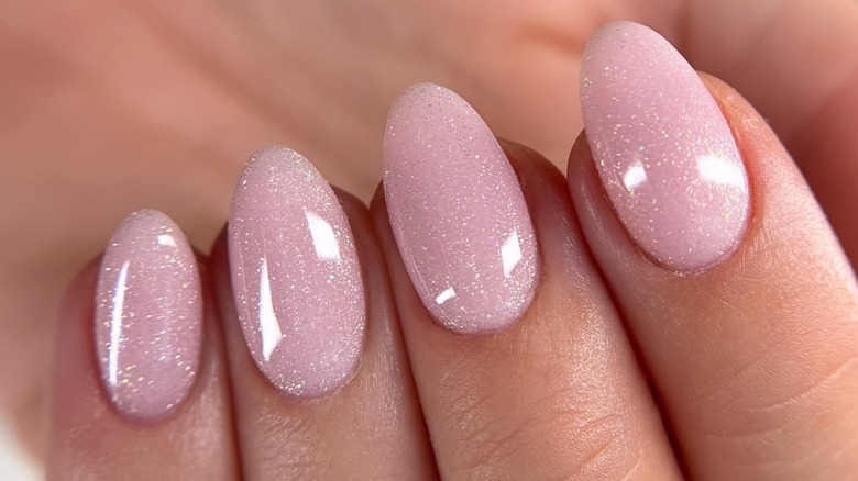 Doigts sur une main avec une peau fraîche et tonique avec une manucure rose givrée et scintillante